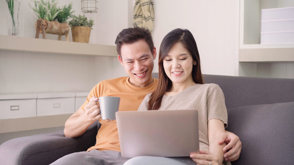 This image has an empty alt attribute; its file name is asian_couple_using_laptop_drinking_warm_cup_coffee_living_room_home-1024x576.jpg
